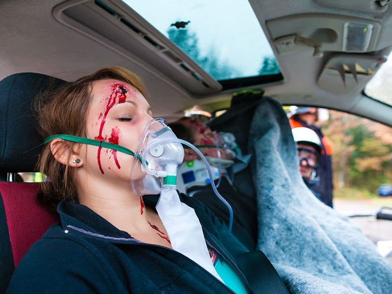 A woman with blood on her face is lying in the back seat of a car.