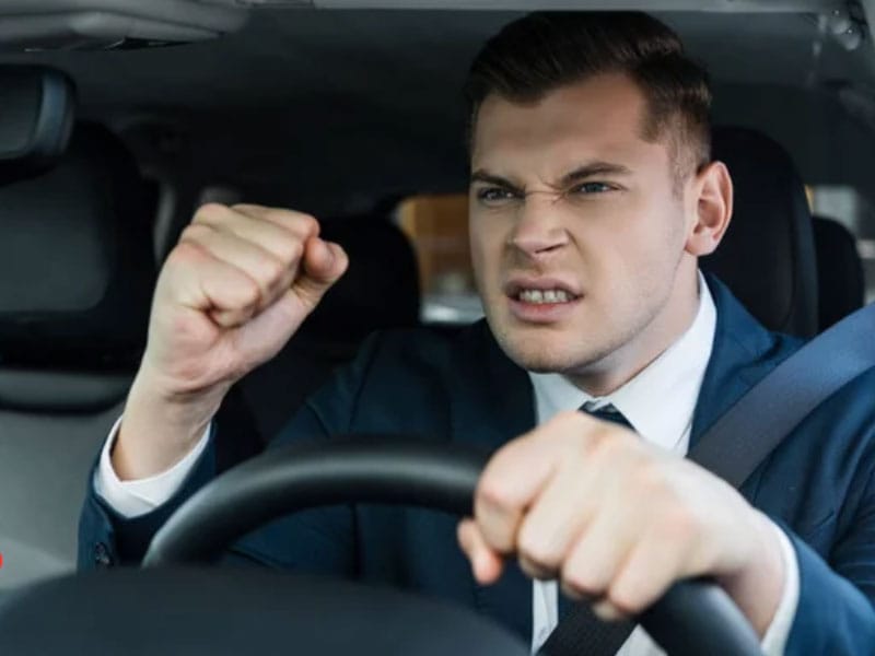 A man in a suit driving a car with his fists up.