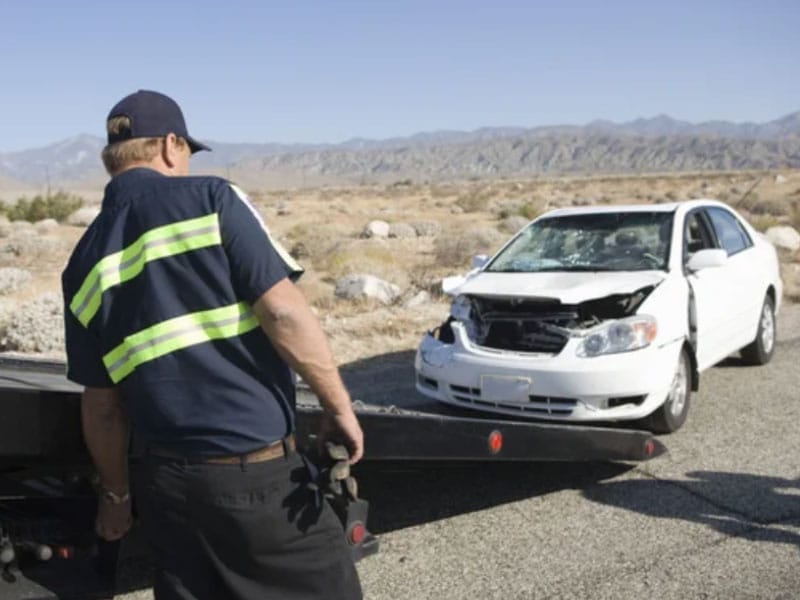 Un hombre está de pie junto a un coche que ha sido atropellado por una grúa.