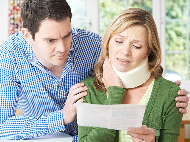 Man comforting a woman wearing a neck brace as they both look at a document on How to Find the Best Accident Lawyer in Phoenix.