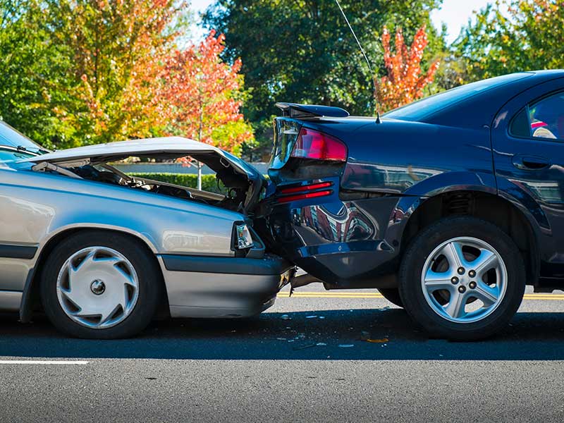 Dos coches implicados en una colisión trasera en una carretera con follaje otoñal al fondo.