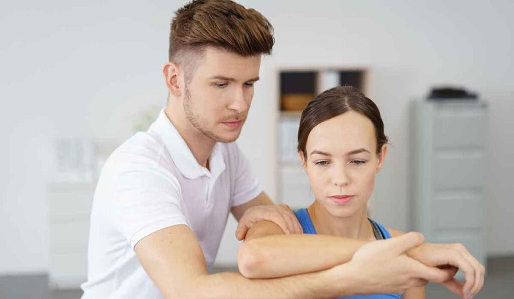 A physical therapist guides a woman through an arm exercise in a clinical setting.